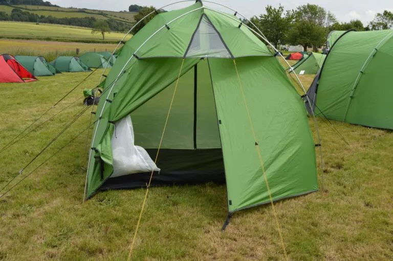 Green camping tent set up in a grassy field, featuring an open entrance and surrounded by other tents, ideal for outdoor enthusiasts and camping trips.