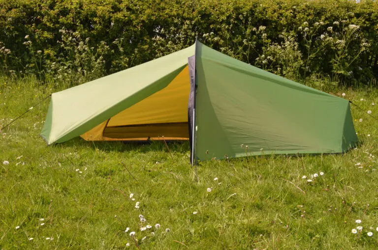 Green and yellow camping tent set up on grassy ground, surrounded by greenery, ideal for outdoor adventures and camping trips.