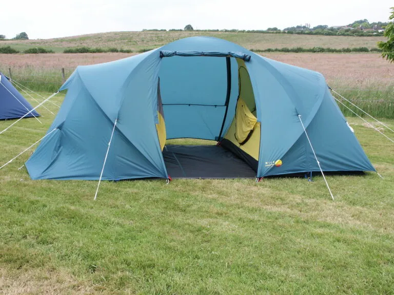 Spacious blue camping tent set up on grassy terrain, featuring an open entrance and bright yellow interior, ideal for outdoor adventures and family camping trips.