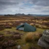 Tent set up in a scenic outdoor landscape featuring rocky hills and moorland under a cloudy sky, ideal for camping and nature exploration.