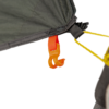 Close-up of an orange plastic hook clipped to a red webbing loop on the corner of a dark green tent fly, with a yellow guyline attached to a black strap and a tent pole visible at the right