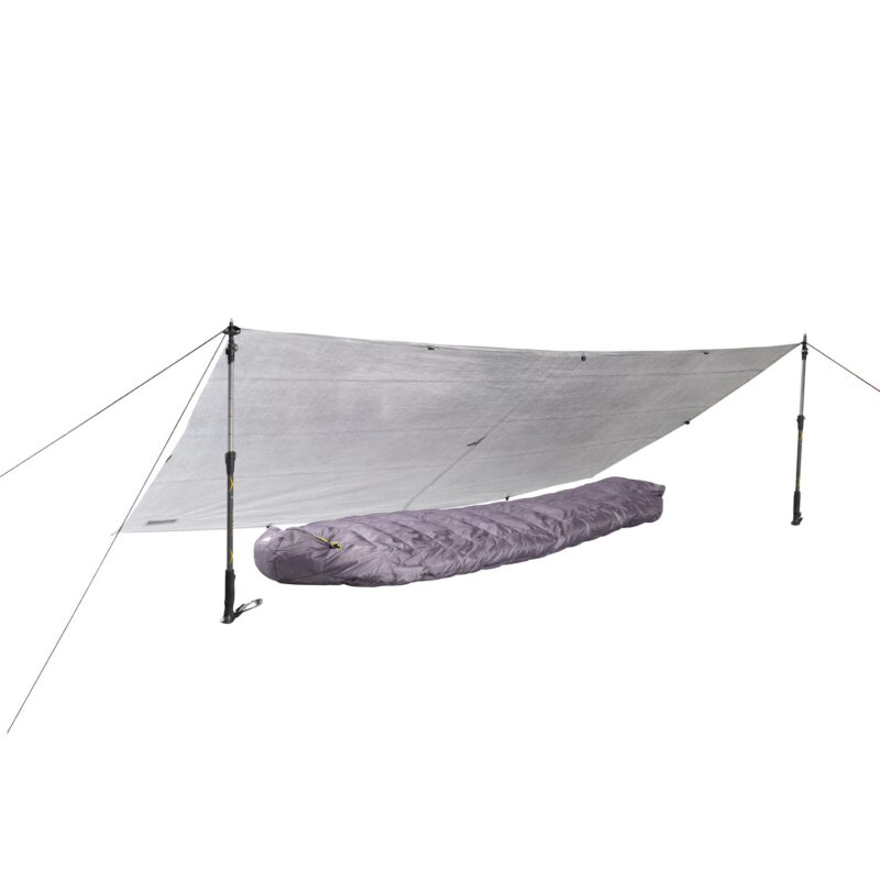 Silver emergency tarp pitched as a low shelter using two adjustable trekking poles and guylines, covering a purple mummy-style sleeping bag beneath.
