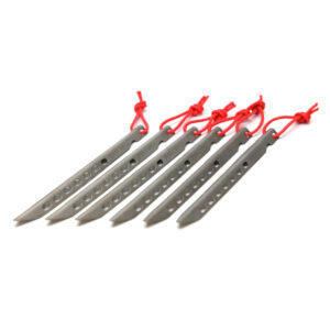 Six slim grey metal tent pegs with pointed tips and rows of oval holes, each fitted with a knotted red cord loop, arranged diagonally on a white background.