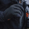 Close-up of a person's hand wearing a black outdoor glove, showcasing its stylish design and functionality for cold weather activities. The glove is part of a weather-resistant jacket ensemble, ideal for hiking or winter sports.