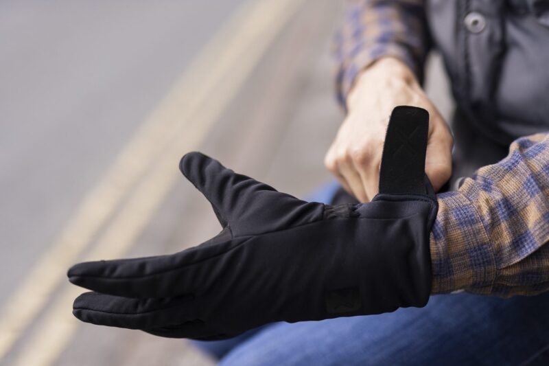 Close-up of a person fastening the Velcro strap of a black glove over their wrist while wearing a blue-and-brown checked shirt, with blurred road lines in the background.