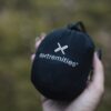 Hand holding a small black drawstring stuff sack stamped with a white "extremities" logo against a blurred green outdoor background.