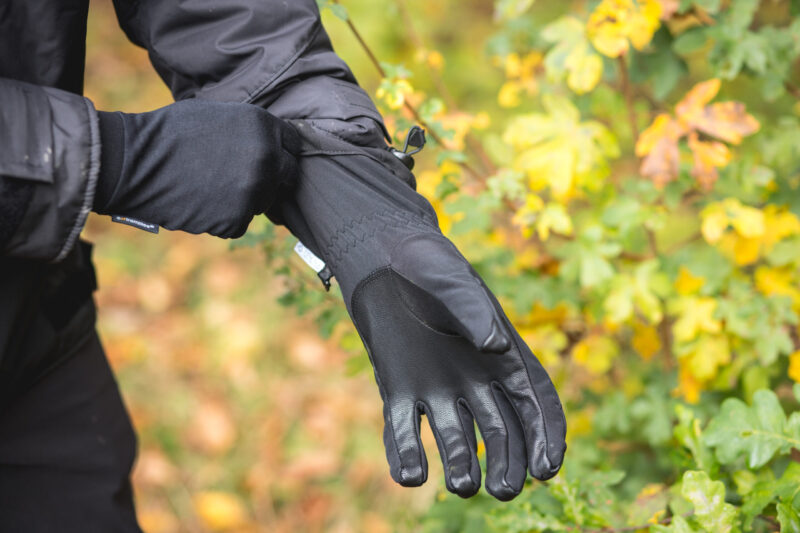 Black gardening gloves being worn by a person, with colorful foliage in the background, showcasing durability and grip for outdoor tasks.