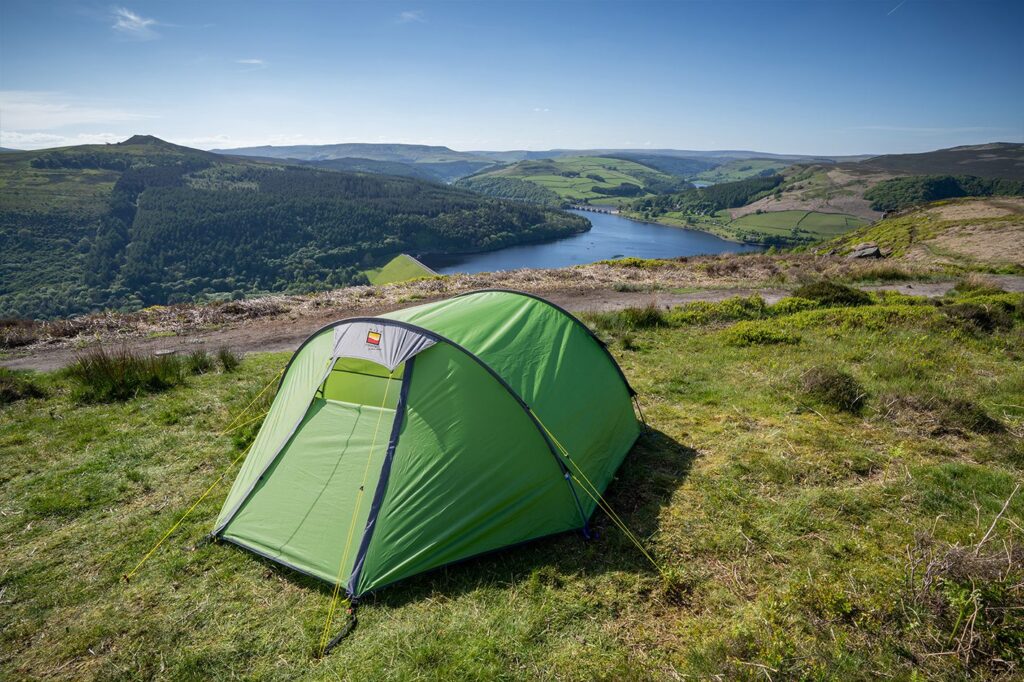 Halcyon-2-3.jpg Bright green dome tent pitched on a grassy hillside overlooking a winding reservoir, wooded valleys and rolling green hills beneath a clear blue sky.