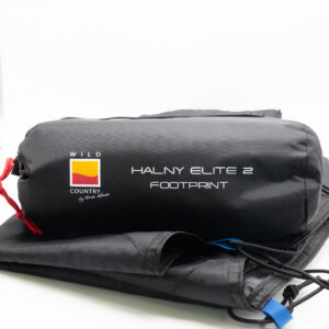 Black cylindrical storage bag marked "WILD COUNTRY" and "HALNY ELITE 2 FOOTPRINT", cinched with a red cord and resting on folded black tent fabric.
