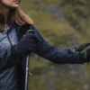 Close-up of a woman wearing gloves and a jacket, holding a hiking pole while exploring a mountainous landscape. The image captures the spirit of outdoor adventure and hiking gear essentials.