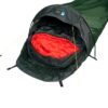 Green single-person bivvy-style tent with a black hood and yellow guy lines, its entrance open to reveal a bright red sleeping bag inside
