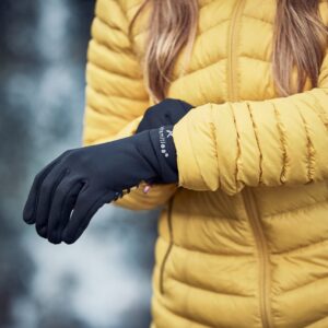 Person wearing a yellow puffer jacket sliding on black winter gloves, hands and jacket in sharp focus against a blurred outdoor background.
