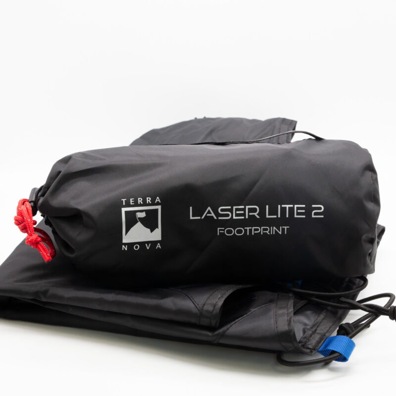 Black rolled storage bag labelled Terra Nova Laser Lite 2 Footprint with a red drawcord, resting on folded black fabric that shows a blue tab and elastic cords