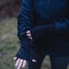 Person outdoors wearing a navy jacket and black thumb‑hole gloves, adjusting one sleeve with their hands visible against a blurred grassy background.