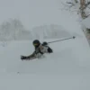 Skier navigating deep powder snow during a winter storm, showcasing dynamic skiing technique amidst a snowy landscape.
