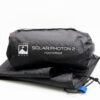Black packed storage bag printed with 'Terra Nova Solar Photon 2 Footprint' resting on folded black footprint fabric with a visible blue webbing pull tab and drawcord.