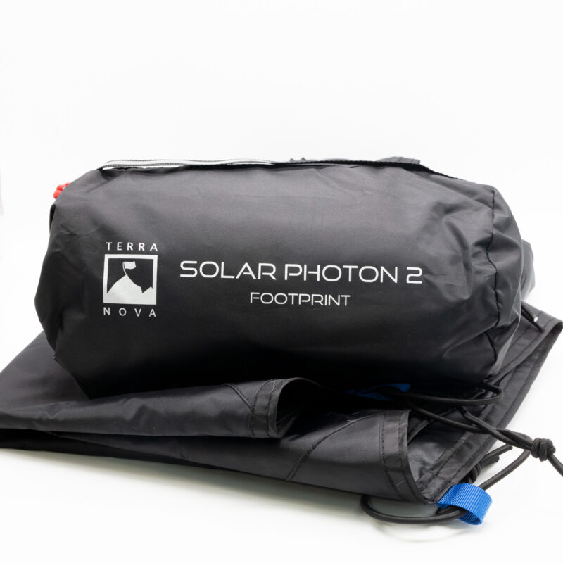 Black packed storage bag printed with 'Terra Nova Solar Photon 2 Footprint' resting on folded black footprint fabric with a visible blue webbing pull tab and drawcord.
