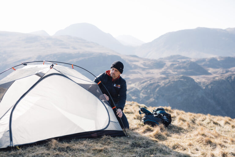Man setting up a tent in a mountainous landscape, showcasing camping gear and outdoor adventure.