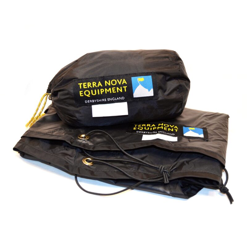 Black Terra Nova Equipment stuff sack with yellow logo patch and small mountain icon sitting on a folded black waterproof sheet showing brass grommets and a knotted drawcord
