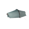 Low-profile two-person tunnel tent in muted teal-green with a black arched pole, taut flysheet and pegged guy lines photographed against a white background.