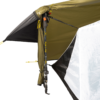 Close-up of a tent corner with an olive-green rainfly and white inner panel, propped open by a carbon-pattern trekking pole and secured with yellow guy lines and adjustment straps.