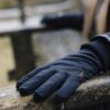 Close-up of a black gloved hand resting on a weathered wooden bench, showing padded fabric, a small orange logo on the glove and a blurred outdoor background.