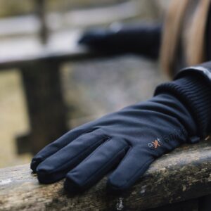 Close-up of a black gloved hand resting on a weathered wooden bench, showing padded fabric, a small orange logo on the glove and a blurred outdoor background.