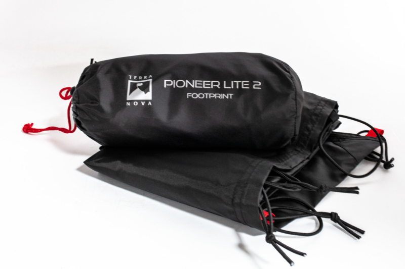 Compressed black stuff sack labelled 'Terra Nova PIONEER LITE 2 FOOTPRINT' with a red drawcord, resting beside folded black groundsheet fabric on a white background.