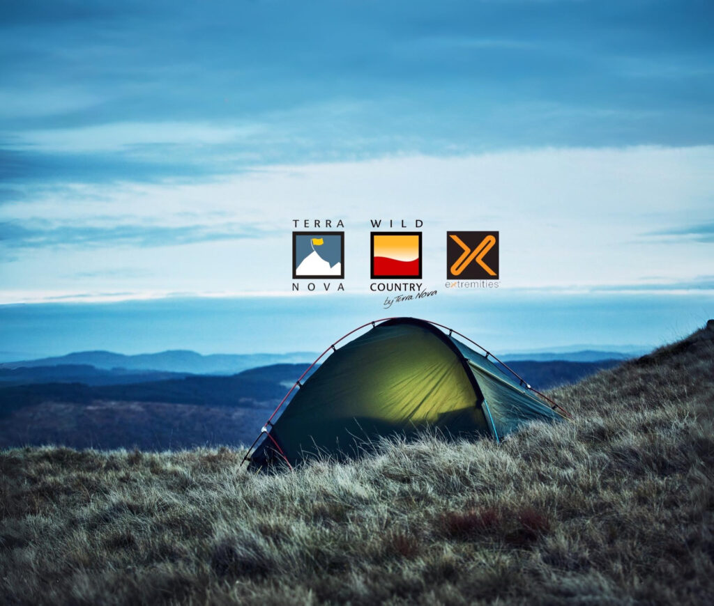 A glowing green tent pitched on a windswept grassy hillside at dusk with layered blue hills and a cloudy sky in the background, and three outdoor brand logos (Terra Nova, Wild Country, Extremities) centred above it