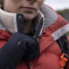 Close-up of a person wearing a red puffer jacket and a black glove, adjusting their collar outdoors, showcasing winter apparel and outdoor gear suitable for cold weather activities.