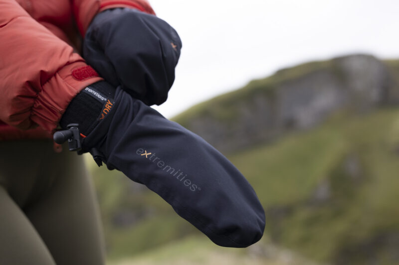 Close-up of a person wearing insulated outdoor mittens in a rugged landscape, showcasing the durable fabric and design ideal for cold weather activities.