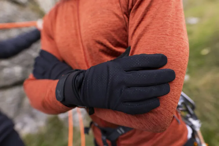 Close-up of a person wearing black gloves, crossing their arms over an orange jacket, ideal for outdoor activities in cold weather.